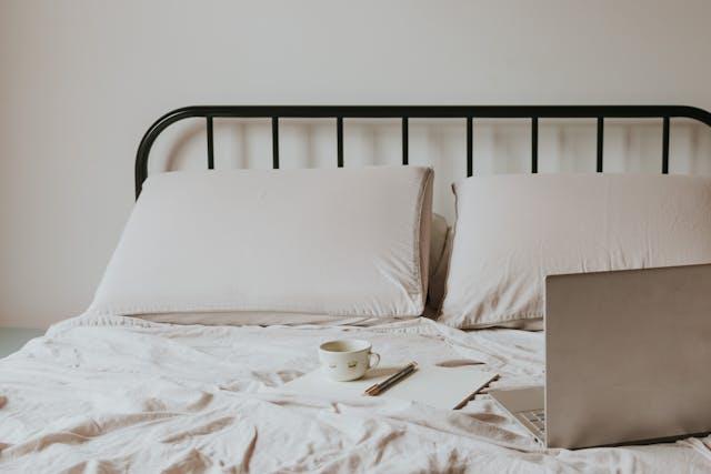 A bed with a black metal frame, soft bedding, and a laptop on the bed, perfect for small living spaces